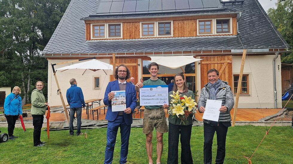 Glückwunsch zum Sanierungspreis 2025: Bürgermeister Martin Seltmann (l.) und Torsten Wenzel (r.), Filialdirektor Deutsche Bank, überreichen das Preisgeld an die Bauherren Stefan Leitner und Lilly Koppatsch. 