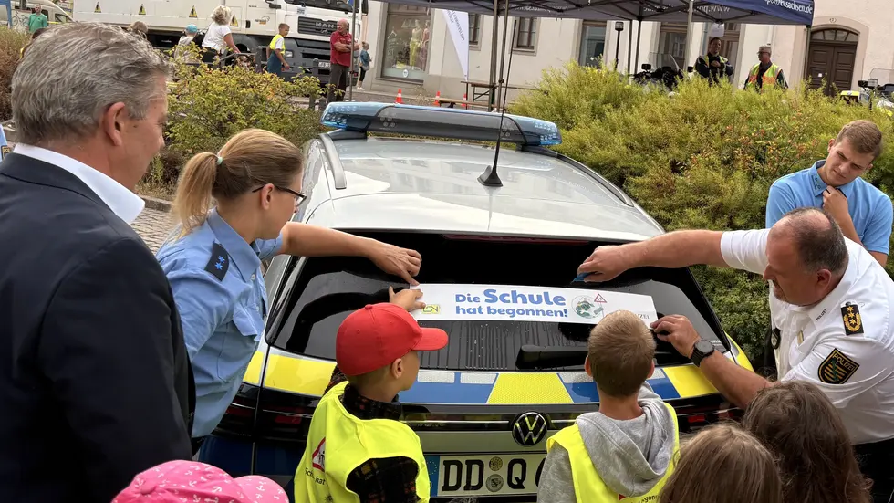 Polizeipräsident René Demmler klebt gemeinsam mit ABC Schützen "Achtung" Sticker auf Autos und Busse.