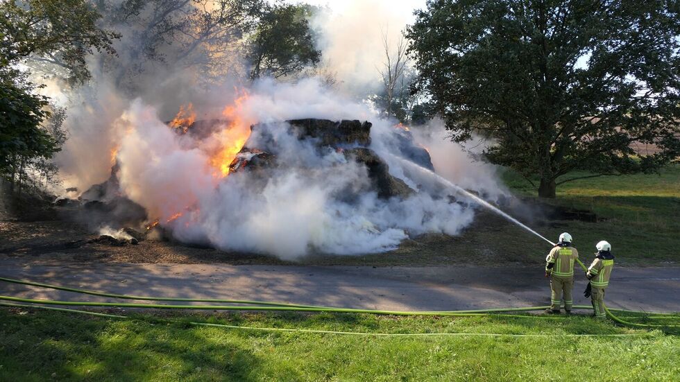 Feuerwehrleute halten den Schlauch auf den brennenden Strohhaufen.